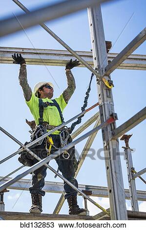 Stock Image - Caucasian worker on scaffolding on construction site. Fotosearch
