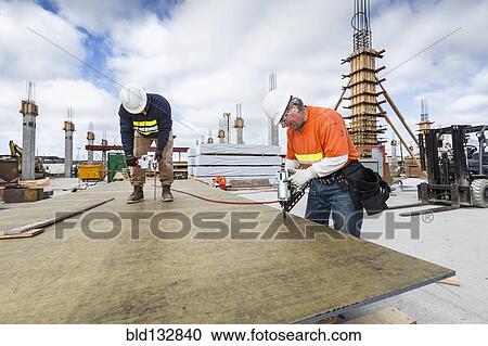 Stock Image - Caucasian workers drilling plant at construction site. Fotosearch