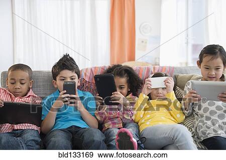 Stock Photo - Children using technology on sofa. Fotosearch