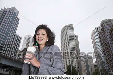 Stock Image - Chinese businesswoman drinking coffee on city street. Fotosearch