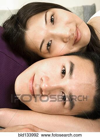Stock Image - Chinese couple relaxing on bed. Fotosearch