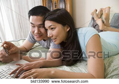 Chinese couple using laptop on bed View Large Photo Image Stock Image - Chinese couple using laptop on bed. Fotosearch