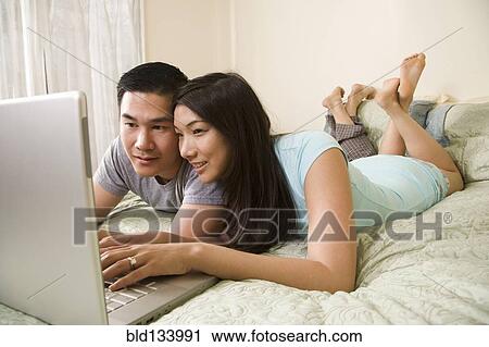 Stock Image - Chinese couple using laptop on bed. Fotosearch