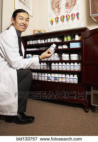 Chinese medicine practitioner selecting herbs from cabinet View Large Photo Image Stock Photo - Chinese medicine practitioner selecting herbs from cabinet. Fotosearch