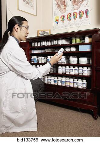 Stock Photograph - Chinese medicine practitioner selecting herbs from cabinet. Fotosearch