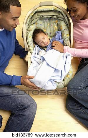 Stock Photo - Couple admiring baby in car seat. Fotosearch