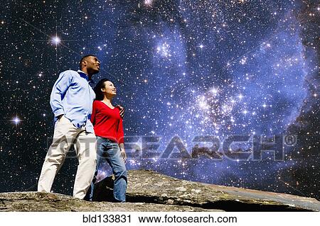 Stock Image - Couple admiring galaxy from rock formation. Fotosearch
