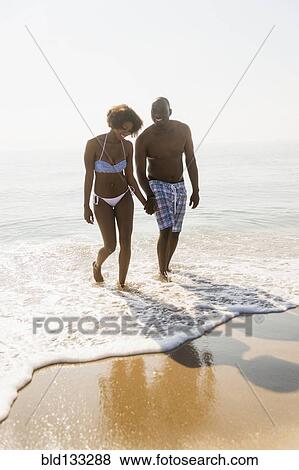 Stock Photo - Couple holding hands in waves on beach. Fotosearch