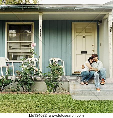 Stock Image - Couple hugging on front stoop of house. Fotosearch