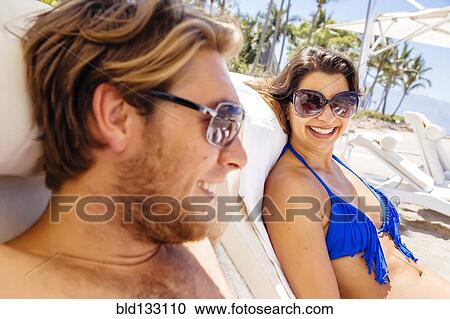 Stock Image - Couple relaxing in lounge chairs on beach. Fotosearch