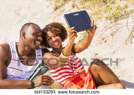 Stock Image - Couple taking pictures with digital tablet on beach. Fotosearch