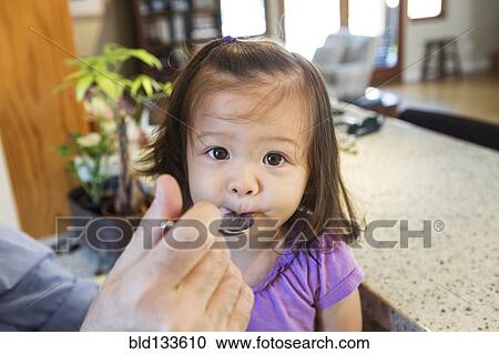 Stock Image - Father feeding daughter in kitchen. Fotosearch
