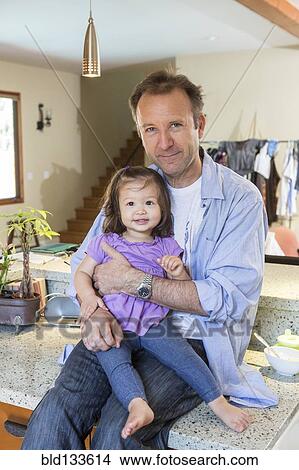 Picture - Father holding daughter in kitchen. Fotosearch