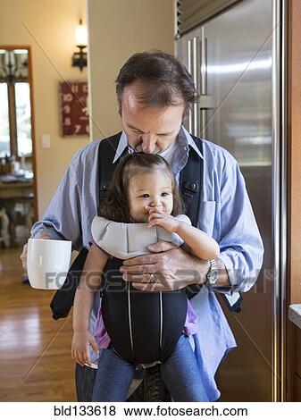 Stock Photo - Father holding daughter in sling in kitchen. Fotosearch