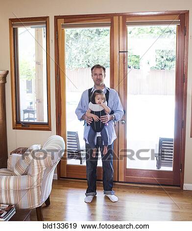 Stock Photo - Father holding daughter in sling in living room. Fotosearch