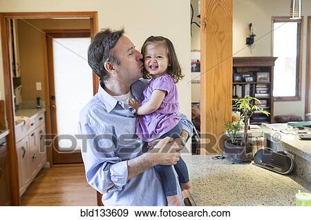 Stock Photo - Father kissing daughter in kitchen. Fotosearch