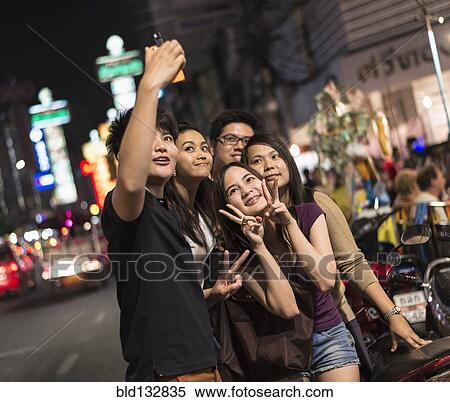 Stock Photography - Friends taking pictures on city street at night. Fotosearch