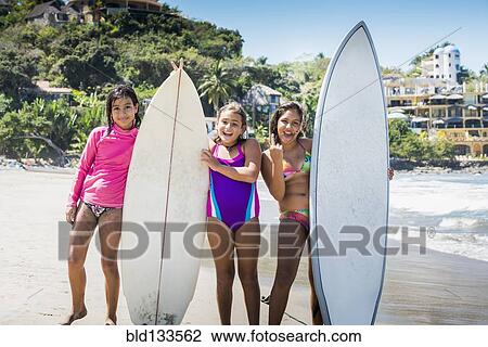 Stock Image - Girls holding surfboards on beach. Fotosearch