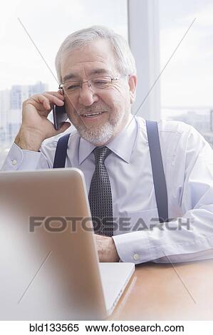 Stock Photography - Hispanic businessman talking on cell phone at desk. Fotosearch