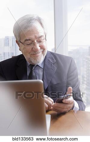 Hispanic businessman using cell phone at desk View Large Photo Image Stock Image - Hispanic businessman using cell phone at desk. Fotosearch