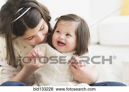 Stock Photo - Hispanic girl holding toddler sister in living room. Fotosearch
