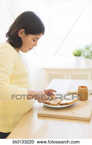 Stock Image - Hispanic girl making peanut butter sandwich. Fotosearch