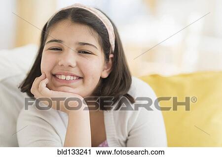 Stock Image - Hispanic girl smiling on sofa. Fotosearch