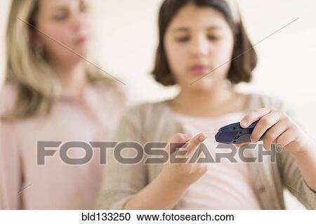Stock Image - Hispanic girl testing her blood sugar. Fotosearch