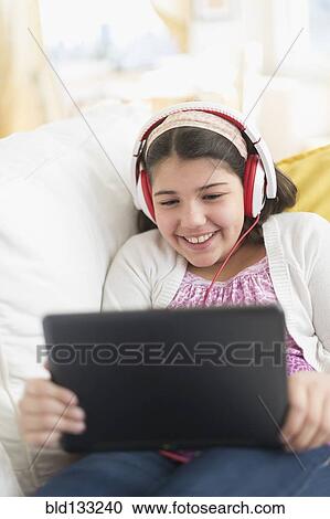 Stock Image - Hispanic girl using digital tablet on sofa. Fotosearch