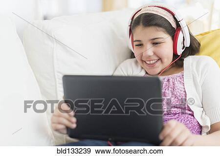 Stock Photo - Hispanic girl using digital tablet on sofa. Fotosearch