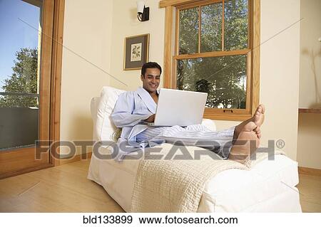 Stock Photo - Hispanic man using laptop in armchair. Fotosearch