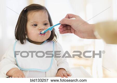 Stock Photo - Hispanic mother feeding toddler in high chair. Fotosearch