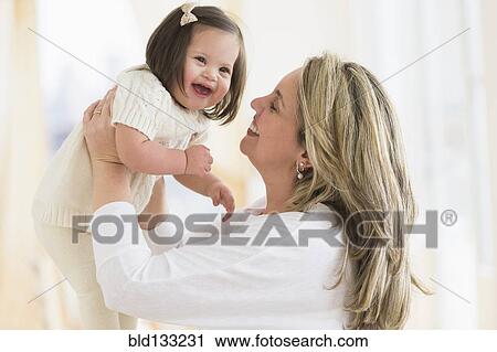 Stock Image - Hispanic mother playing with daughter in living room. Fotosearch