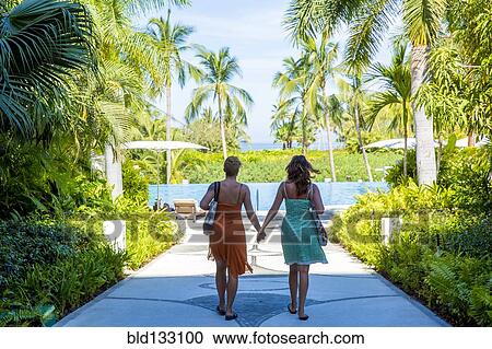 Stock Image - Lesbian couple holding hands at tropical resort. Fotosearch