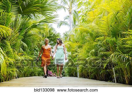 Stock Photo - Lesbian couple holding hands on tropical walkway. Fotosearch