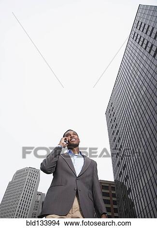 Mixed businessman talking on cell phone on city street View Large Photo Image Picture - Mixed businessman talking on cell phone on city street. Fotosearch