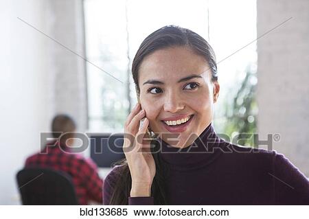 Stock Photography - Mixed race architect talking on cell phone in office. Fotosearch