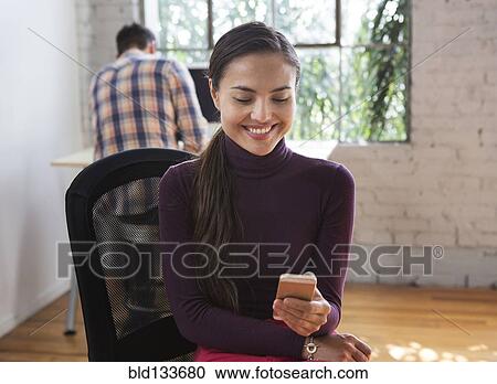 Stock Image - Mixed race architect using cell phone in office. Fotosearch