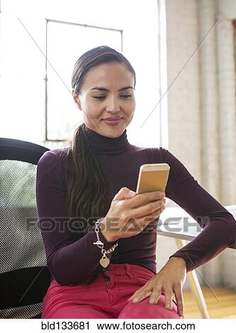 Stock Image - Mixed race architect using cell phone in office. Fotosearch