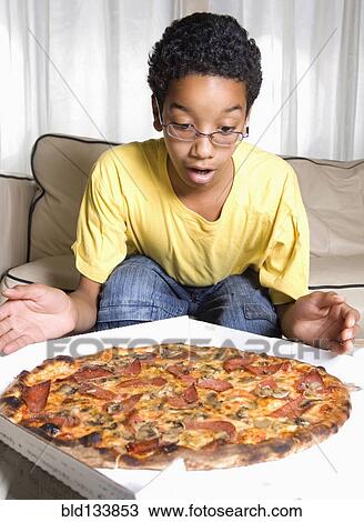 Mixed race boy admiring pizza in living room View Large Photo Image Stock Image - Mixed race boy admiring pizza in living room. Fotosearch
