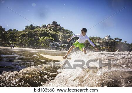 Stock Photo - Mixed race boy surfing in ocean. Fotosearch