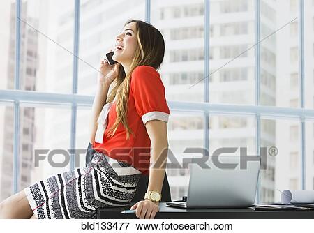 Stock Photo - Mixed race businesswoman talking on cell phone at desk. Fotosearch