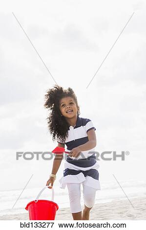 Mixed race girl carrying shovel and bucket on beach View Large Photo Image Stock Photo - Mixed race girl carrying shovel and bucket on beach. Fotosearch