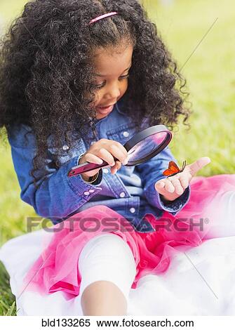 Stock Photography - Mixed race girl examining butterfly with magnifying glass. Fotosearch