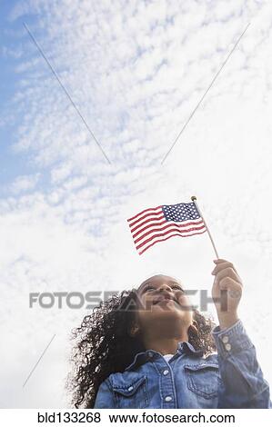 Stock Photo - Mixed race girl holding United States flag outdoors. Fotosearch