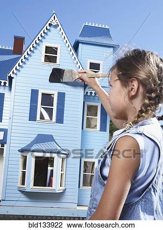 Stock Image - Mixed race girl painting doll house. Fotosearch