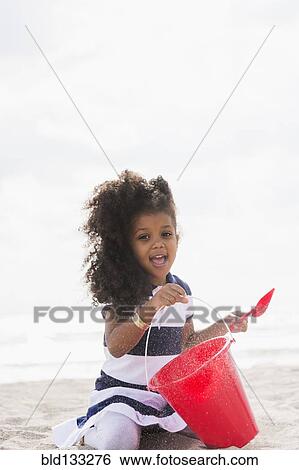 Stock Photograph - Mixed race girl playing in sand on beach. Fotosearch