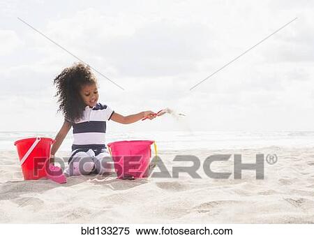 Stock Photography - Mixed race girl playing in sand on beach. Fotosearch