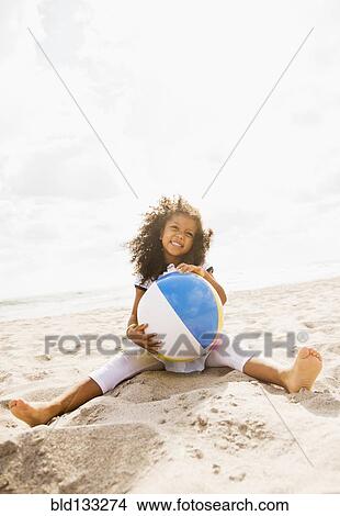 Picture - Mixed race girl playing with ball on beach. Fotosearch