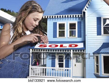 Stock Image - Mixed race girl putting 'sold' sign on doll house. Fotosearch